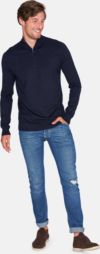 Man met donkerblauwe trui met ritskraag, lachend, staand.
