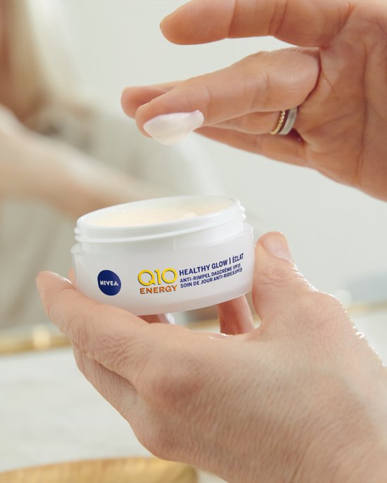 Vrouw met ringen brengt Nivea Q10 Energy dagcrème aan op haar gezicht.