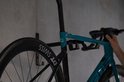 Blauwe racefiets met zwarte velgen hangt aan zwarte fietsmuurbeugel.