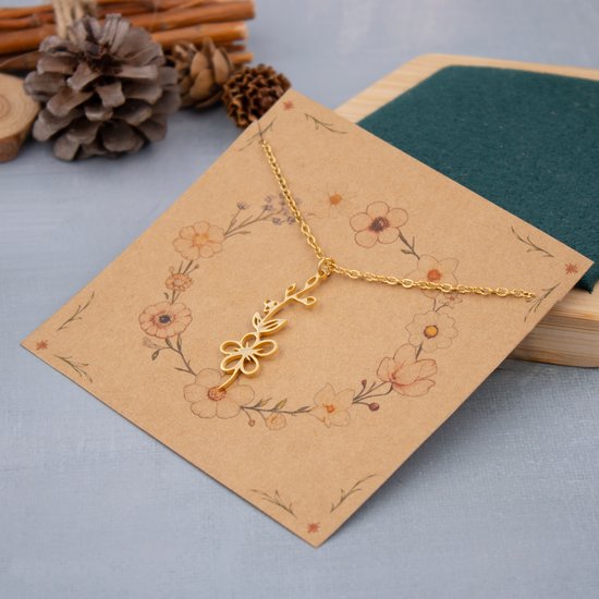 Gouden ketting met bloem- en takjeshanger op een kaart met bloemenkrans.