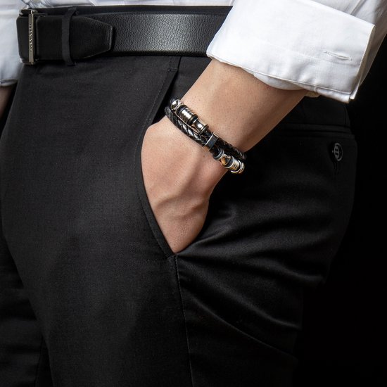 Gevlochten zwarte armband met gouden en zilverkleurige details, gedragen door een man in een wit overhemd.