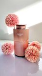 Rose gouden diffuser omringd door lichtroze bloemen, met schaduwen van zonlicht.