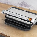 Gesloten Tefal contactgrill op een houten aanrecht. Het bedieningspaneel heeft iconen en een kleurindicator.