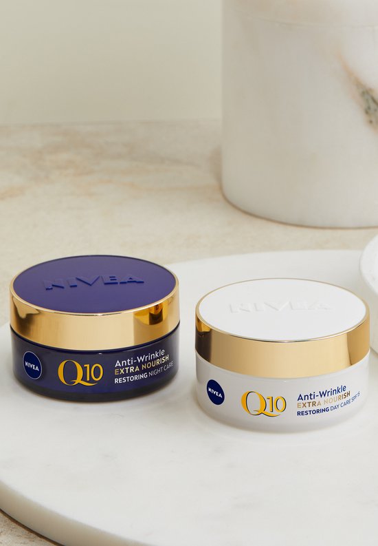 Twee Nivea Q10 potjes, nachtcrème en dagcrème, met gouden deksels, op een marmeren plateau.