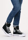 Model in een zwarte Converse Chuck Taylor All Star Lift sneakers met witte veters en een dikke witte zool, gecombineerd met een spijkerbroek.