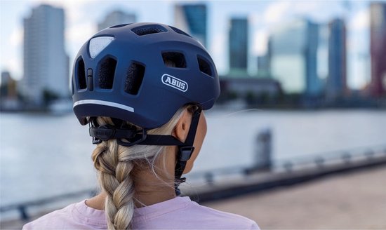 Donkerblauwe fietshelm met reflecterende strepen, gedragen door een vrouw met vlecht.