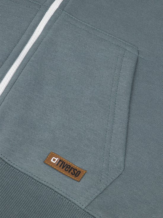 Detail van de kangoeroezak van een blauwgrijze hoodie met een bruin riverso-label.