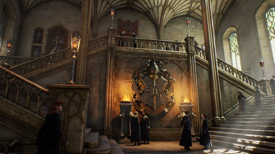 Grand hall avec un escalier en pierre, un blason et des étudiants en robes.