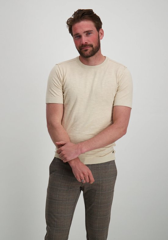 Homme, debout, regardant vers la gauche. T-shirt beige à col rond et manches courtes.