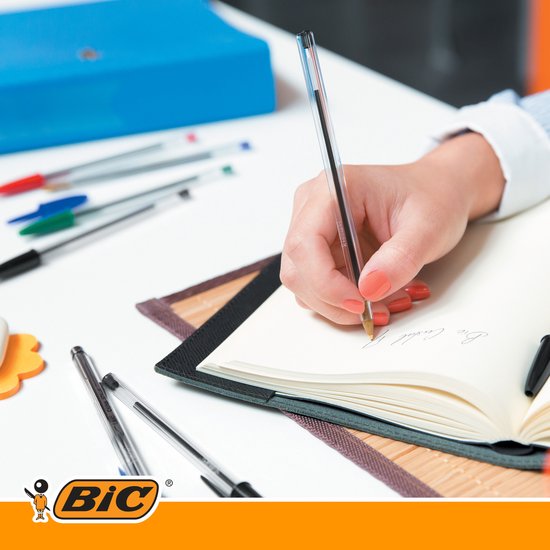 Een hand met rode nagels schrijft in een notitieboekje met een Bic balpen.