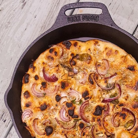 Gietijzeren koekenpan met een gebakken focaccia met rode ui en rozemarijn.