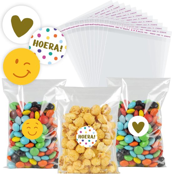 Transparante zakjes met vrolijke stickers: smiley, "Hoera!" en hartjes. Drie zakjes gevuld met snoep en popcorn.