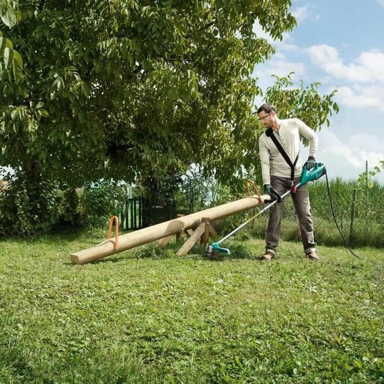 Man gebruikt een elektrische grastrimmer in een grasrijke tuin.