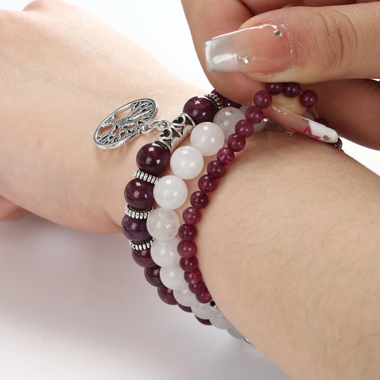 Drie gestapelde armbanden om een pols, met afwisselend paarse en witte kralen en zilverkleurige bedeltjes.