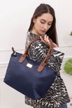 Une femme aux longs cheveux bruns montre un sac en nylon bleu foncé avec des anses en cuir marron.