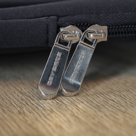 Zilverkleurige ritsen met 'COVERZS' erop, op een donkerblauwe laptoptas.
