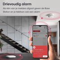 Drievoudige alarmweergave: rookmelder op trap, basisstation op tafel, smartphone met melding 'Smoke Alarm Triggered'.