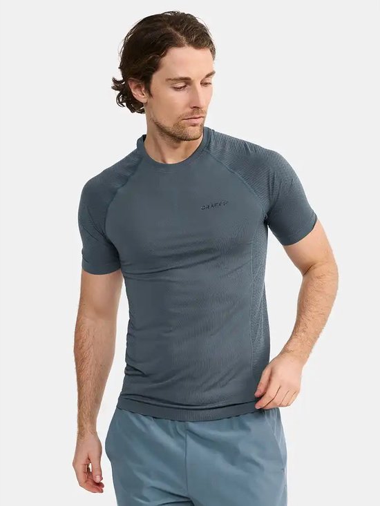 Man in donkergrijs Craft sportshirt met korte mouwen en blauwgrijze sportshort. Gestructureerde stof op schouders en mouwen.