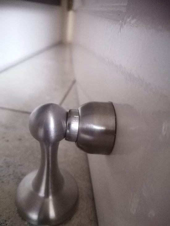 Zilverkleurige deurstopper met magnetische houder, gemonteerd op een witte deur.