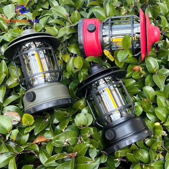 Trois lanternes de camping rouges, vertes et noires, entourées de feuilles vertes.