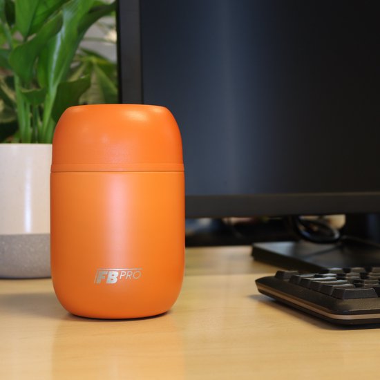 Oranje FB Pro voedselcontainer met een logo op een bureau, naast een computer.