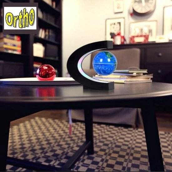 Support noir en forme de C avec un globe flottant sur une table basse, avec des livres et une balle rouge.