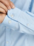 Chemise popeline bleu clair, gros plan sur les poignets boutonnés et la patte de boutonnage.