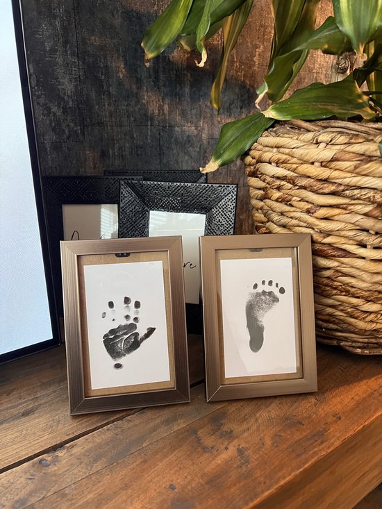 Twee ingelijste afdrukken op een houten ondergrond: een babyhandafdruk en een babyvoetafdruk.