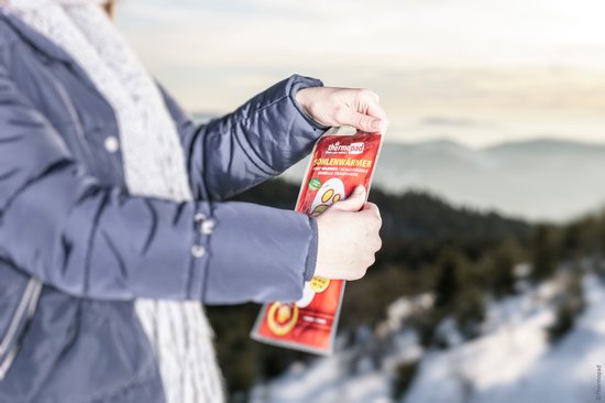 Une femme en vêtements d'hiver ouvre un paquet de semelles chauffantes thermopad dans un paysage enneigé.