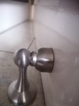 Zilverkleurige, geborstelde metalen deurstopper met bolvormige magnetische kop, gemonteerd op een witte deur.