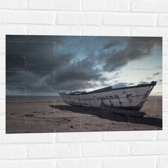 WallClassics - Muursticker - Witte Boot op het Strand onder Donkere Wolken - 75x50 cm Foto op Muursticker