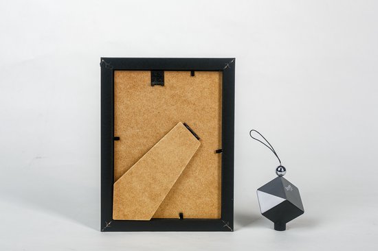 Achterkant van een zwarte fotolijst met standaard en ophangoog. Naast de lijst een decoratief zwart object.