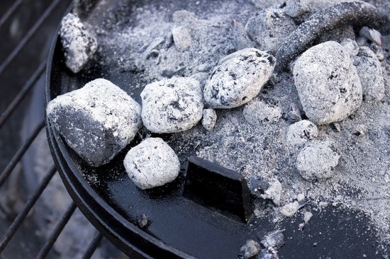 Gloeidende kolen met as op het deksel van een gietijzeren Dutch oven.