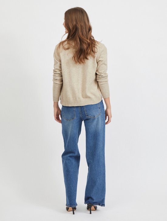 Lichtbeige gebreid vest met lange mouwen, gedragen over een wit shirt en spijkerbroek.