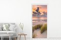 Deursticker met zonsondergang, strand en duingras, naast een grijze bank.