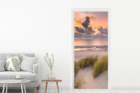 Deursticker met zonsondergang, strand en duingras, naast een grijze bank.