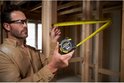 Man met bril meet met gele Stanley FatMax 8m rolbandmaat in houten constructie.