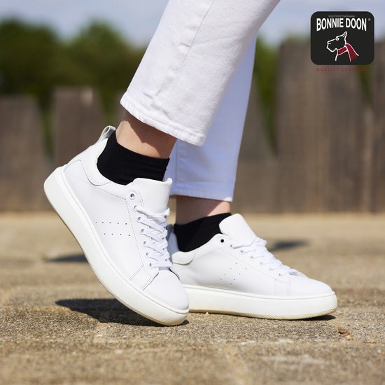 Dames witte leren sneakers met veters, perforaties en dikke zolen. Gedragen met zwarte enkelsokken.
