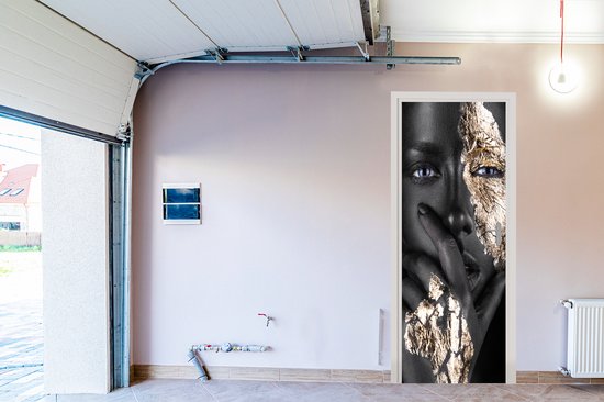 Deursticker van een gezicht, half zwart geschminkt en half bedekt met goudfolie. Blauwe ogen met een mysterieuze blik.
