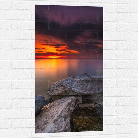 WallClassics - Muursticker - Kleine Rotsen aan het Water met Zonsondergang - 50x100 cm Foto op Muursticker