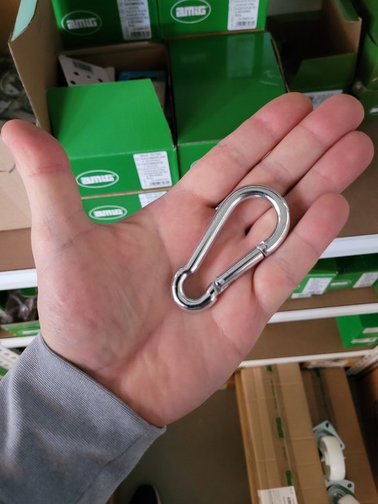 Een hand die een zilverkleurige karabijnhaak vasthoudt, met groene dozen op de achtergrond.