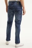 Man met de rug naar de camera, draagt een blauwe spijkerbroek met stonewash-effect en opgerolde pijpen.