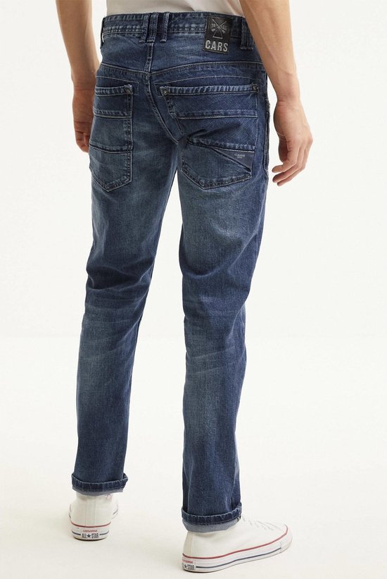 Man met de rug naar de camera, draagt een blauwe spijkerbroek met stonewash-effect en opgerolde pijpen.