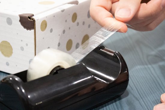 Een zwarte plakbanddispenser met een rol plakband, een hand trekt een stukje plakband eraf.