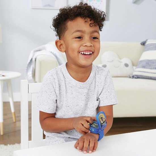 Een jongen met krullend haar lacht en draagt een blauw Paw Patrol horloge dat opengeklapt is.