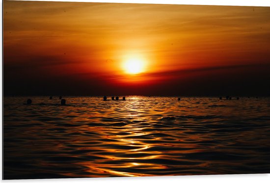 WallClassics - Dibond - Zwemmende Mensen in Zee bij Ondergaande Zon - 105x70 cm Foto op Aluminium (Met Ophangsysteem)