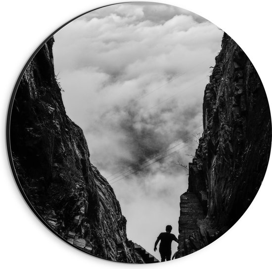WallClassics - Dibond Muurcirkel - Man tussen Rotsen boven Wolken in Zwart-wit - 20x20 cm Foto op Aluminium Muurcirkel (met ophangsysteem)