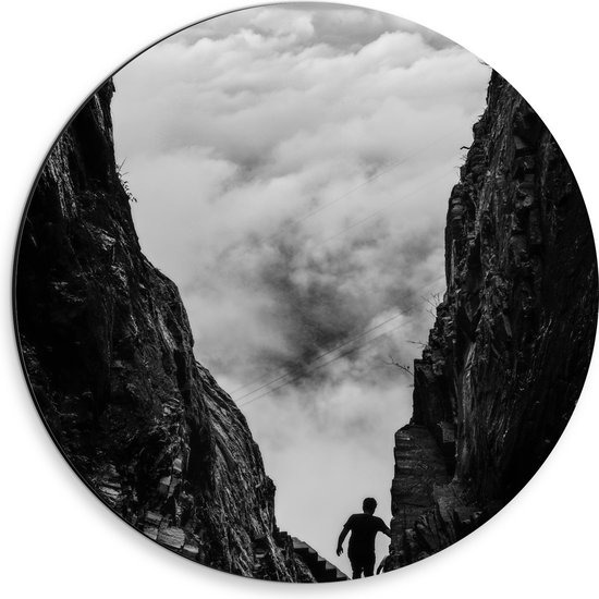 WallClassics - Dibond Muurcirkel - Man tussen Rotsen boven Wolken in Zwart-wit - 30x30 cm Foto op Aluminium Muurcirkel (met ophangsysteem)