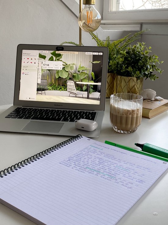 Un bureau avec un ordinateur portable, un carnet, une tasse de café, des écouteurs et des plantes.