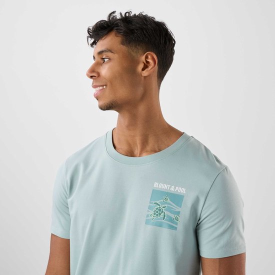 Man in lichtblauwe T-shirt met zeeschildpad-print op de borst, profiel van het gezicht.